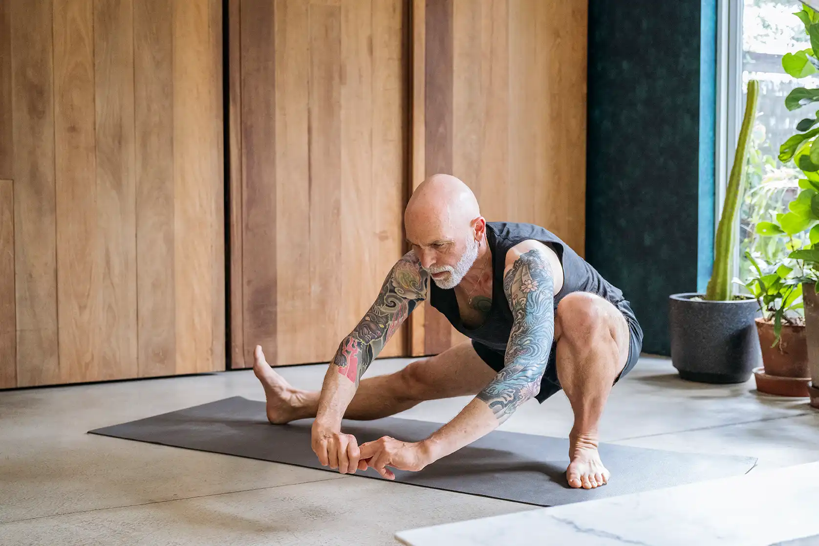 Sportlicher Mann dehnt sich im eigenen Fitnessraum mit Holzverkleidung